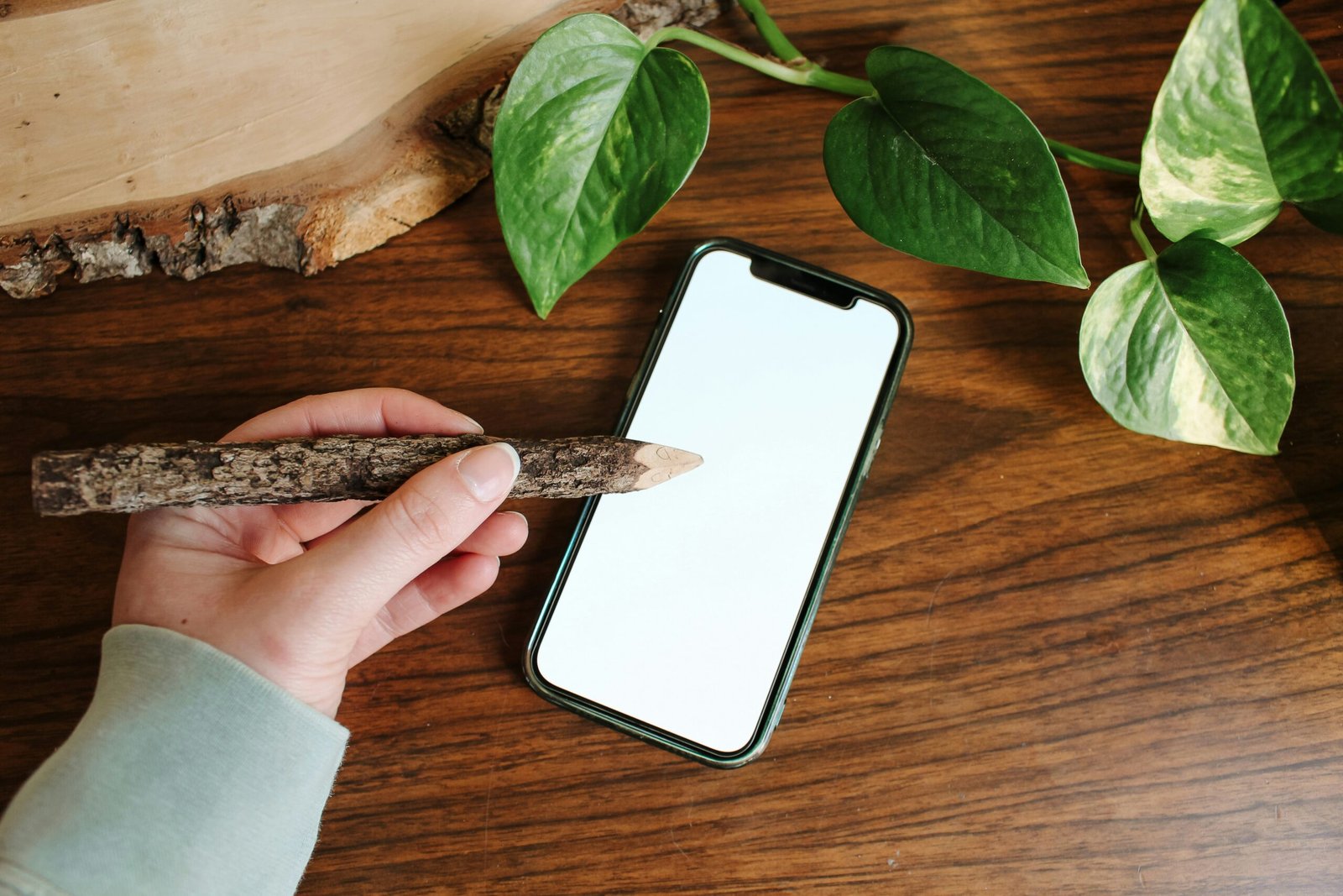 A hand uses a stick to touch a phone.